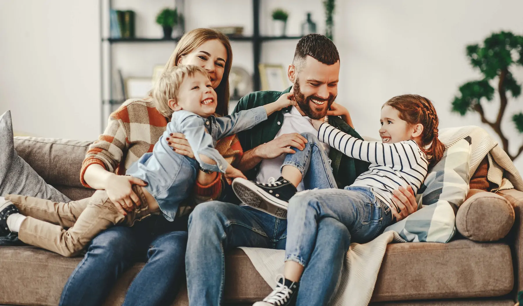 Caucasian mom and dad with son and daughter laughing and smiling on a couch.