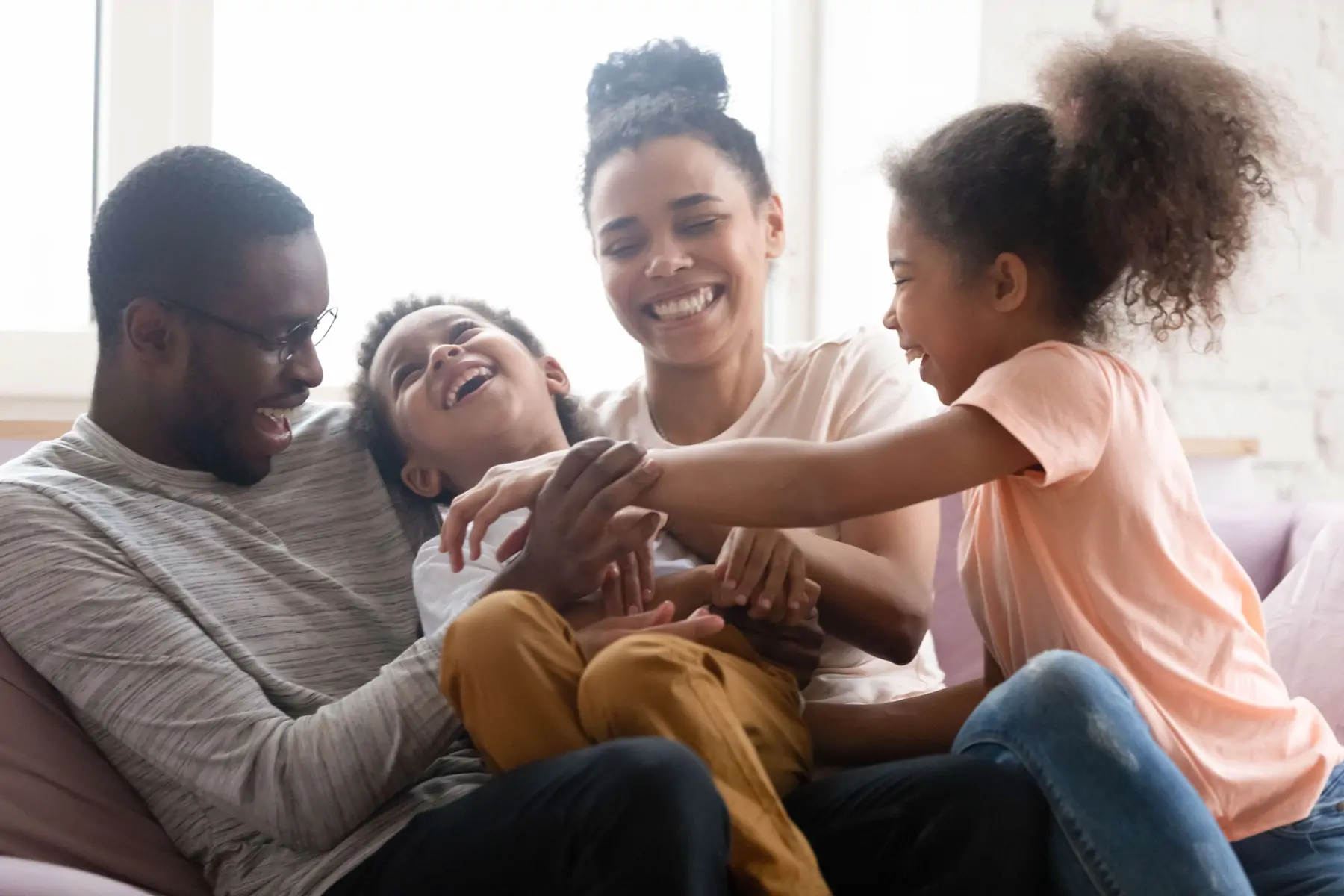 Black mom and dad with son and daughter laughing and smiling on a couch.