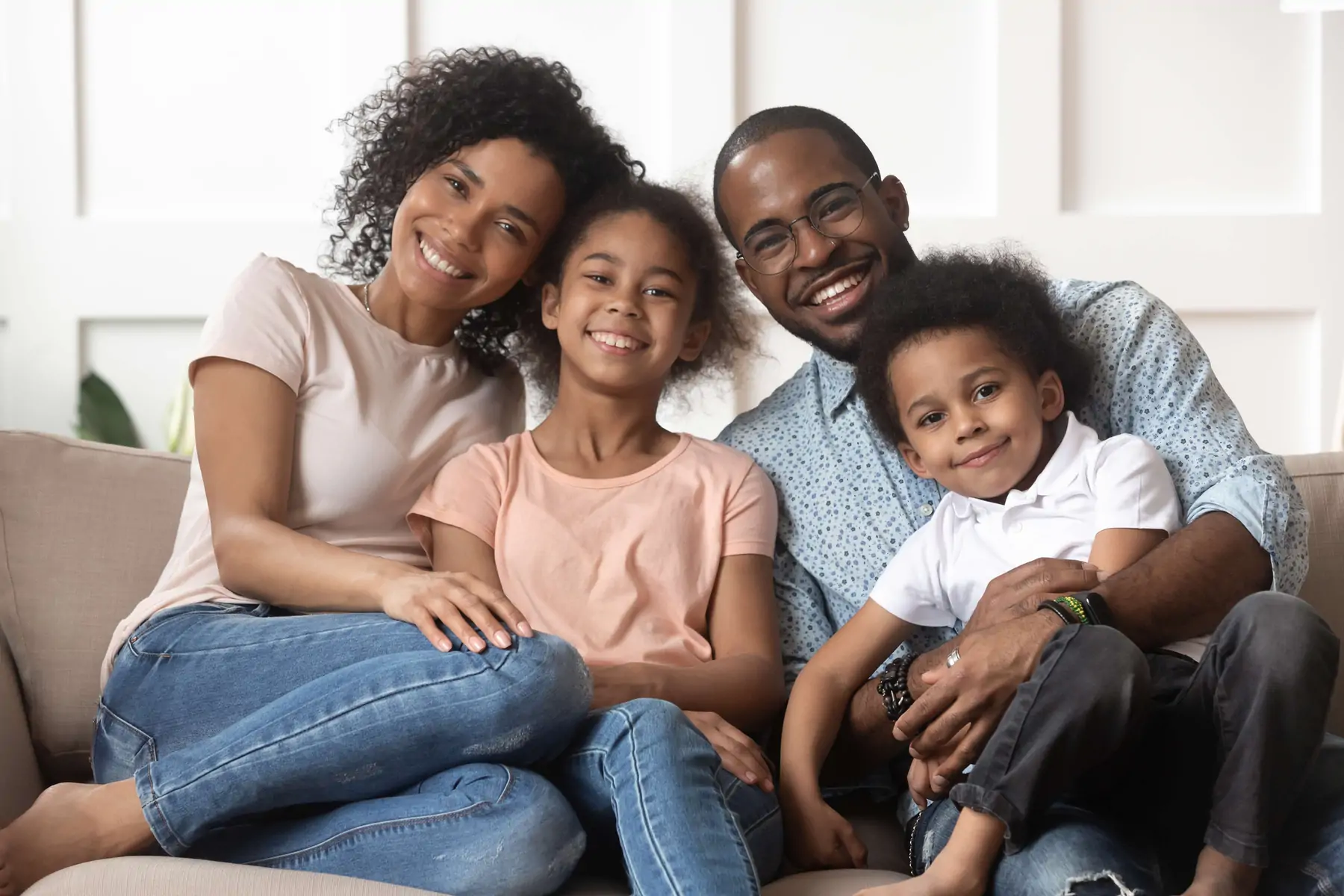 Black mom and dad with son and daughter smiling on a couch.