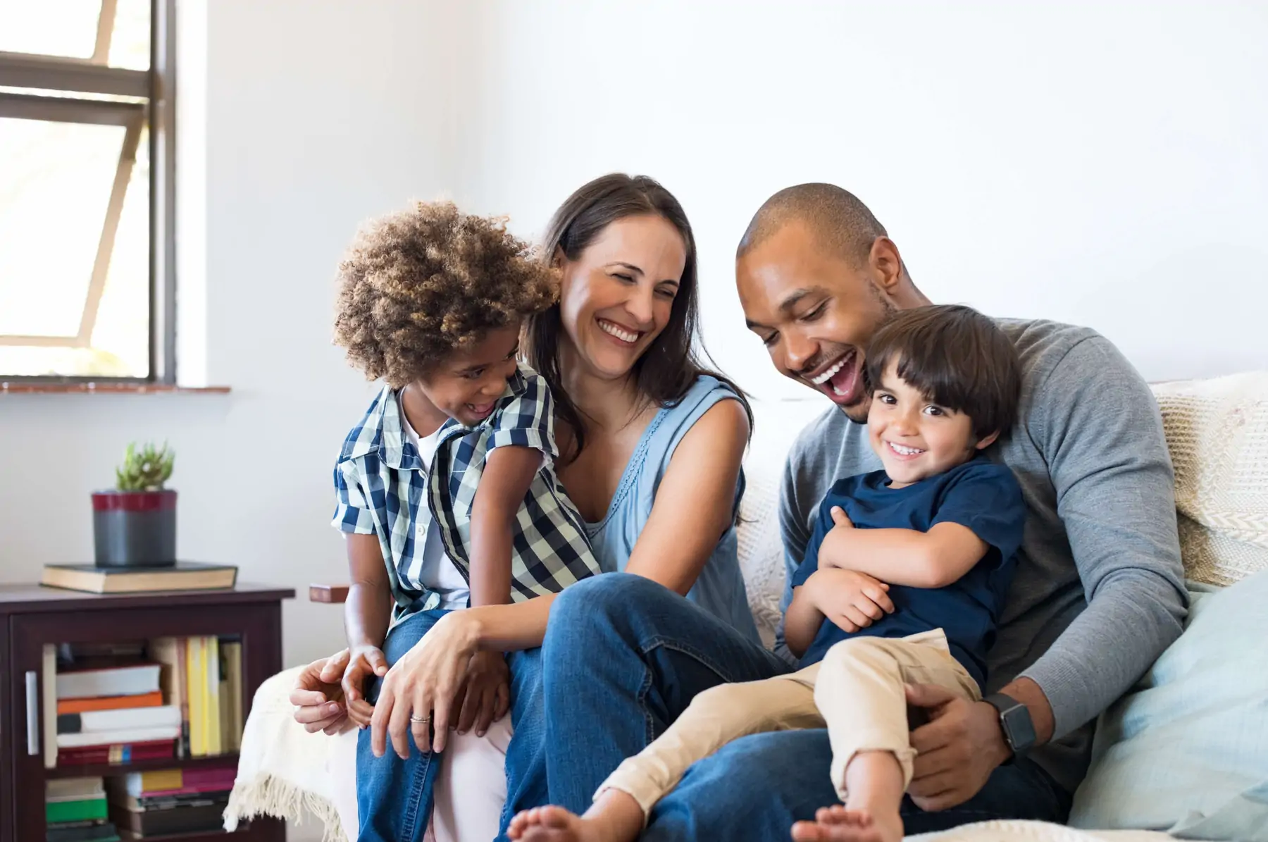 Caucasian mom and black dad with two sons smiling on a couch.