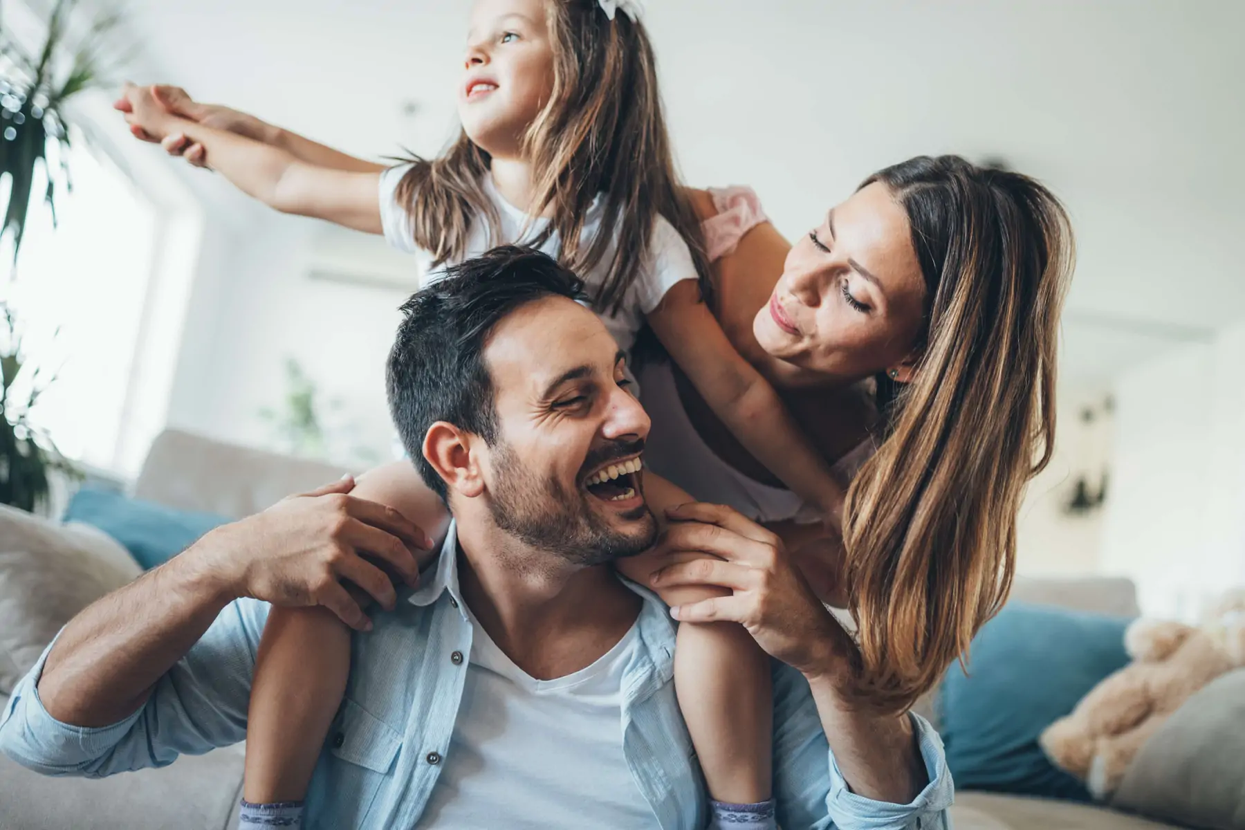 Greek mom and dad with daughter laughing and smiling, while the daughter rides on the dad's shoulders.